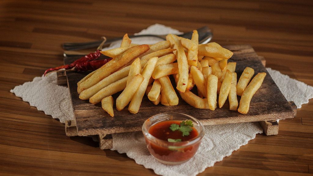 Crispy golden French fries with red dipping sauce fresh cilantro and dried chili peppers on wood Wallpaper
