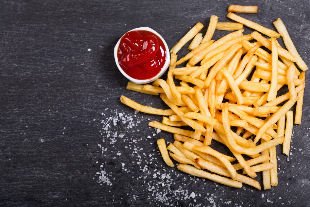 Top-down photo of crispy golden salted French fries with red ketchup on dark slate background Wallpaper