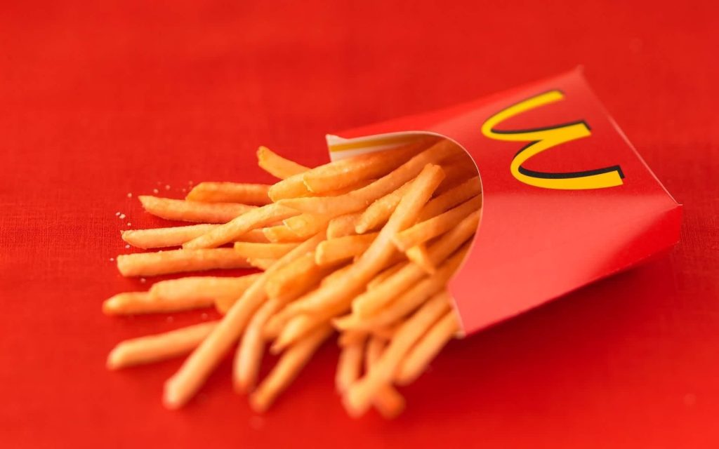 Crispy large McDonalds French fries in classic carton on vibrant red background wallpaper