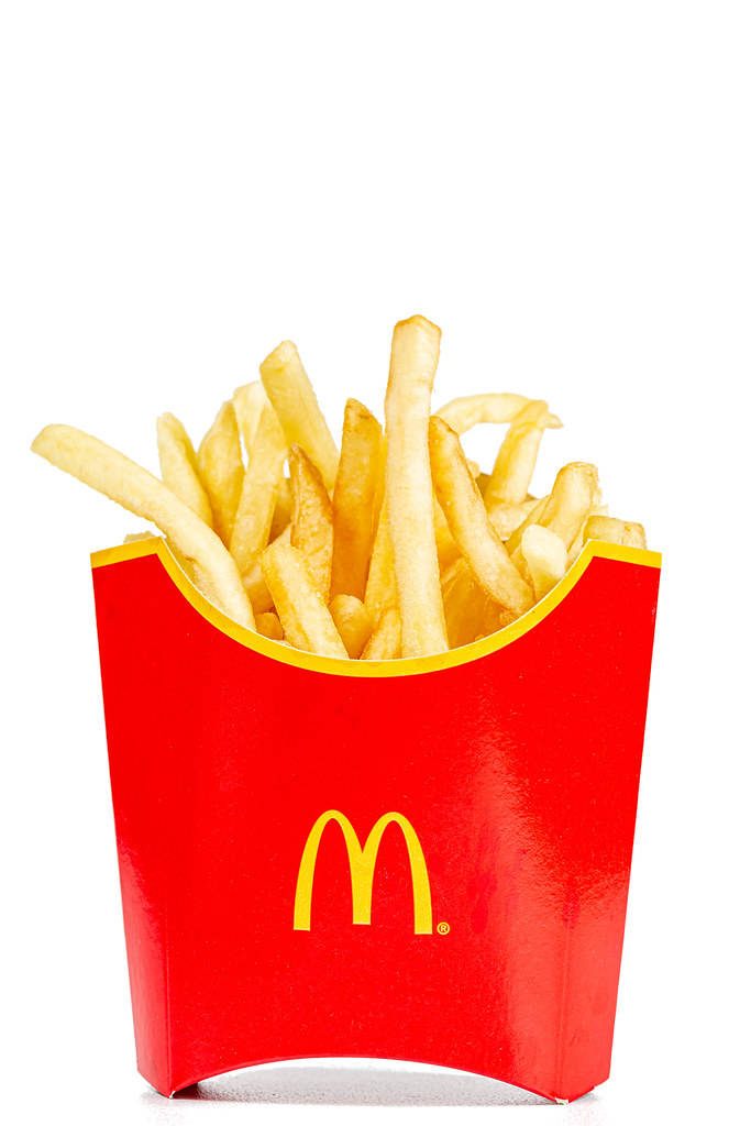 Crispy golden McDonald’s French fries in classic red carton with yellow arches on white background Wallpaper