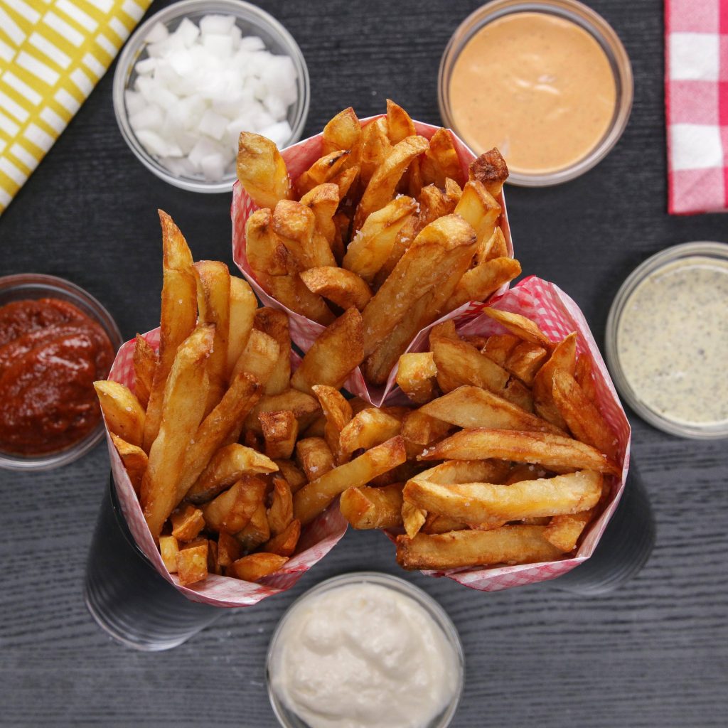 Overhead view of crispy thick-cut fries in checkered cones with colorful dipping sauces Wallpaper