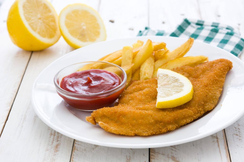 Golden breaded Wiener Schnitzel with French fries lemon wedge and ketchup on rustic white table Wallpaper