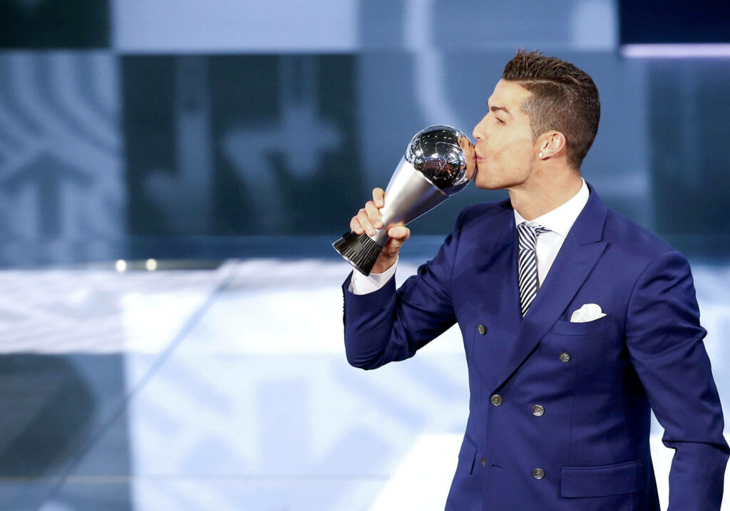 Cristiano Ronaldo in blue suit kissing The Best FIFA Football Award trophy celebrating victory Wallpaper