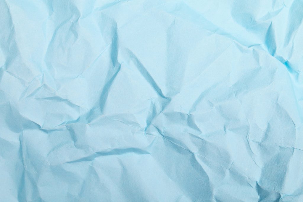 Crumpled pastel blue paper texture with soft folds and natural light minimalist wallpaper background