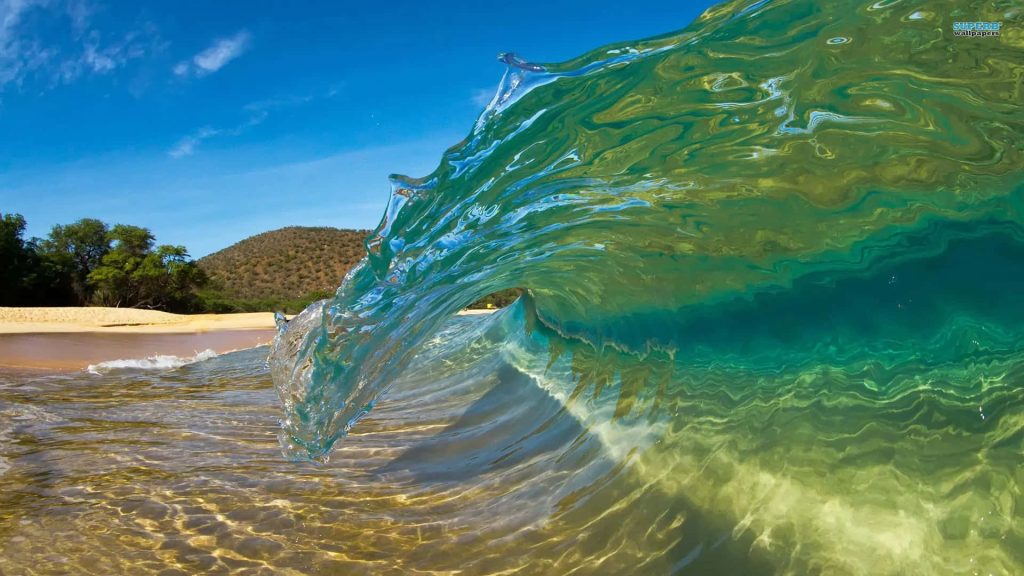 Crystal-clear emerald turquoise wave cresting over tropical sandy beach with sunny caustics Wallpaper