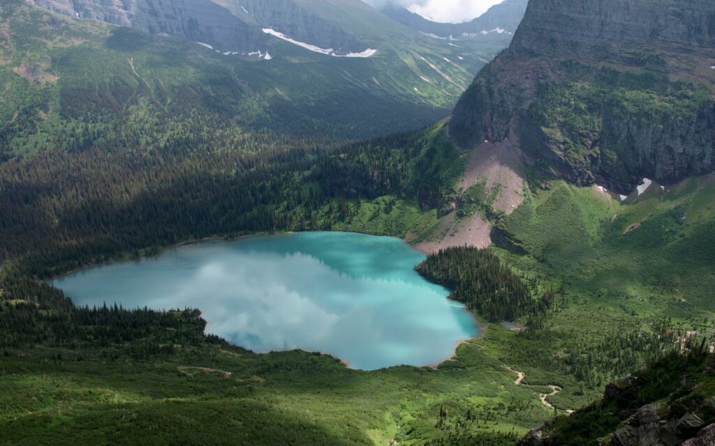 Crystal-clear turquoise lake in lush lowland with dramatic mountains and vibrant green forests wallpaper