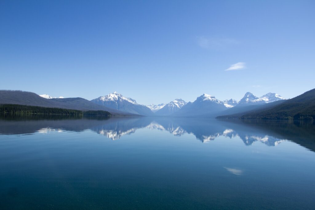Crystal-clear lake reflecting snow-capped mountains under bright blue sky natural landscape wallpaper