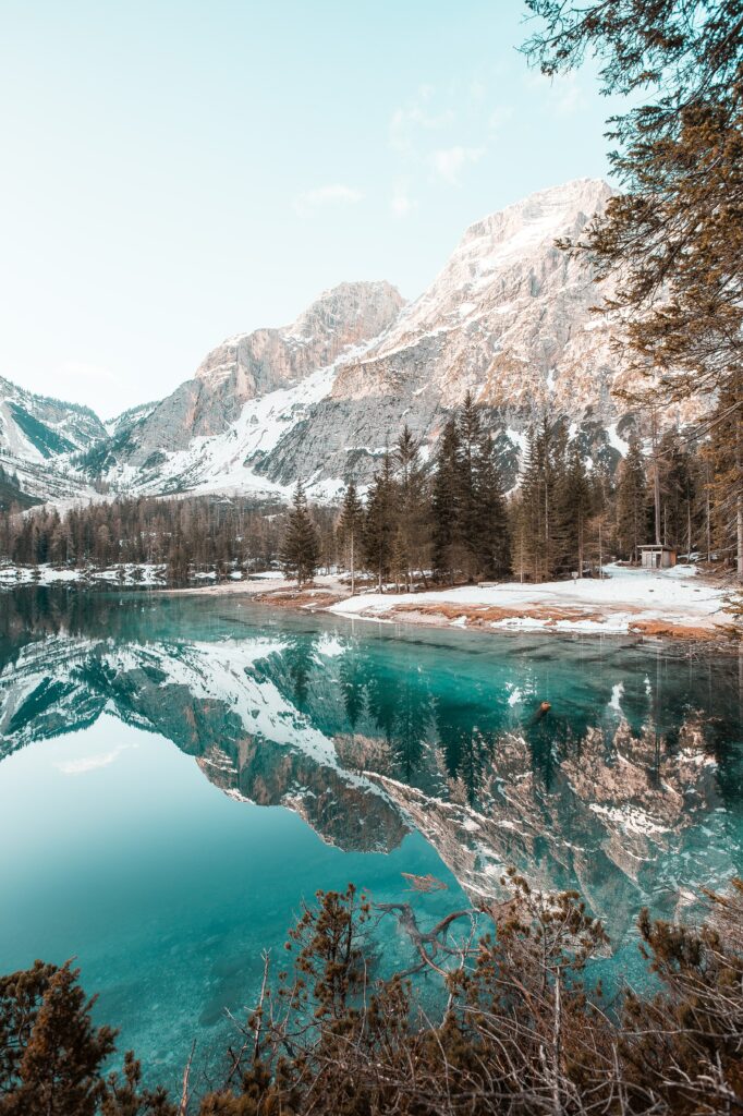 Crystal-clear lake reflecting snow-capped mountains and dense spruce forests under blue sky Wallpaper
