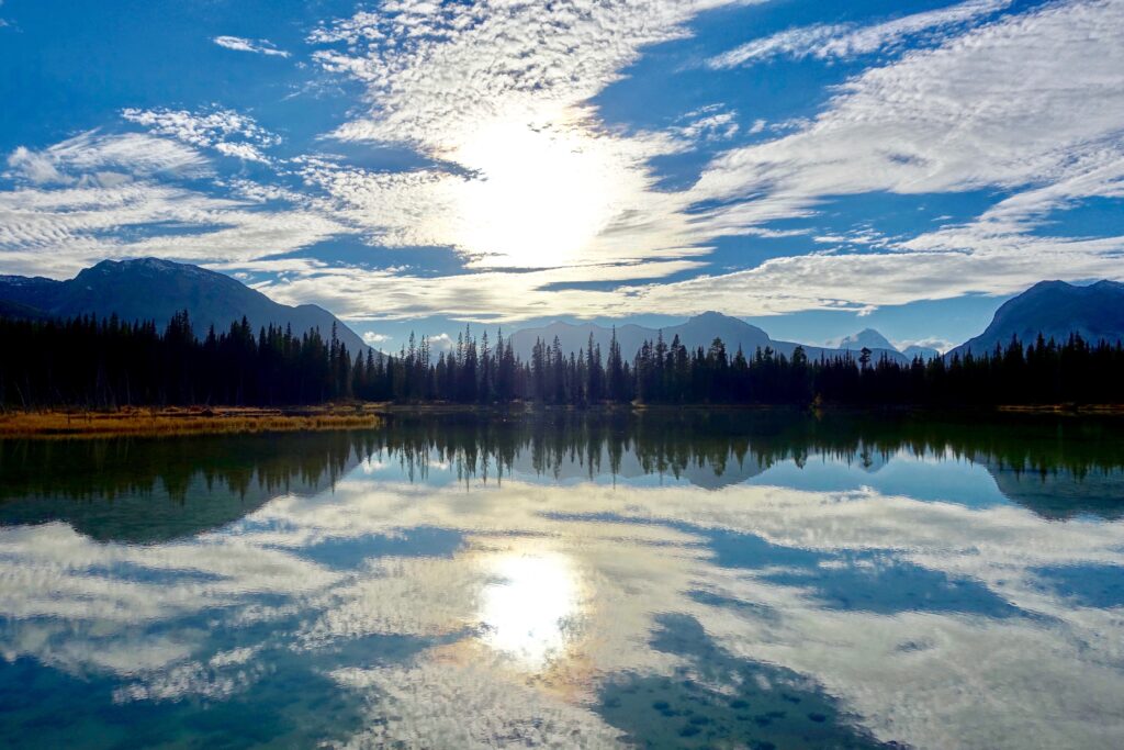 Serene lake reflecting dramatic sky clouds and mountains with lush forest silhouettes wallpaper