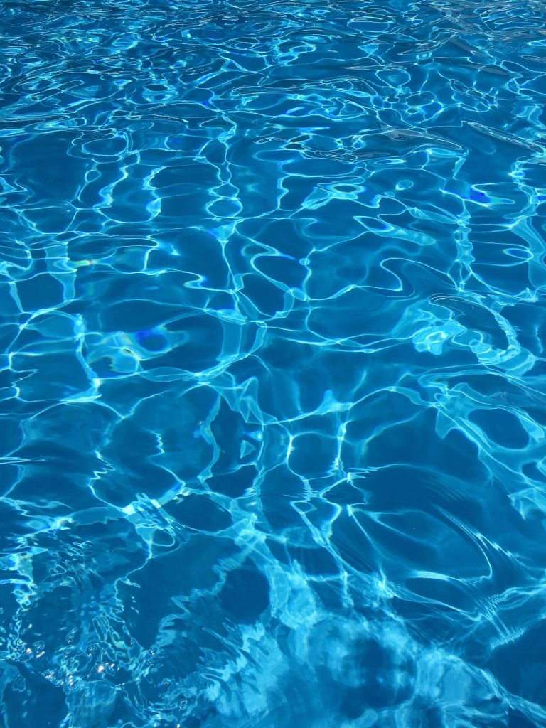 Crystal clear swimming pool water with vibrant ripples and sunlight reflections summer wallpaper background