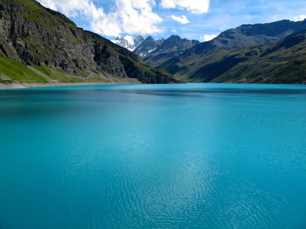 Turquoise lake reflecting majestic mountains lush green slopes dramatic clouds bright blue sky Wallpaper
