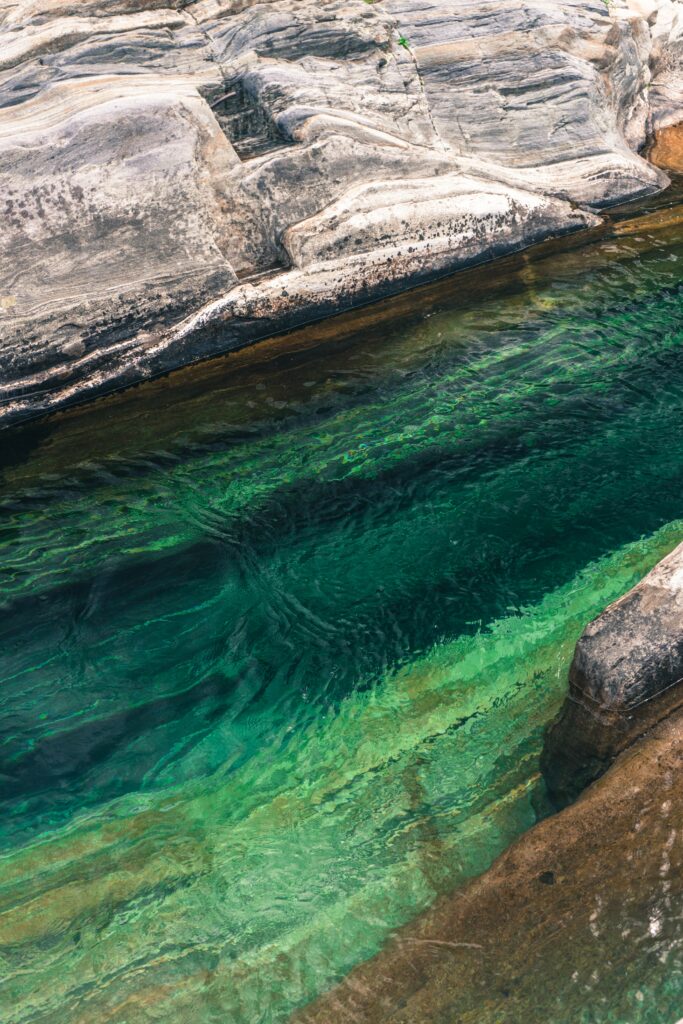 Crystal clear water flowing over smooth layered stones with shimmering green and blue hues wallpaper