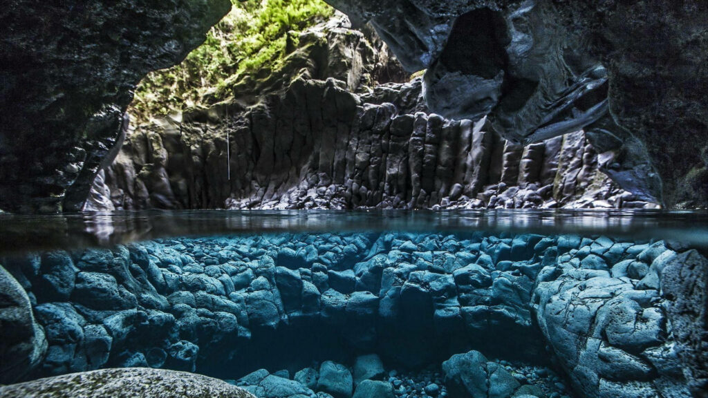 Serene cave interior with basalt columns lush greenery and clear water over volcanic stones wallpaper