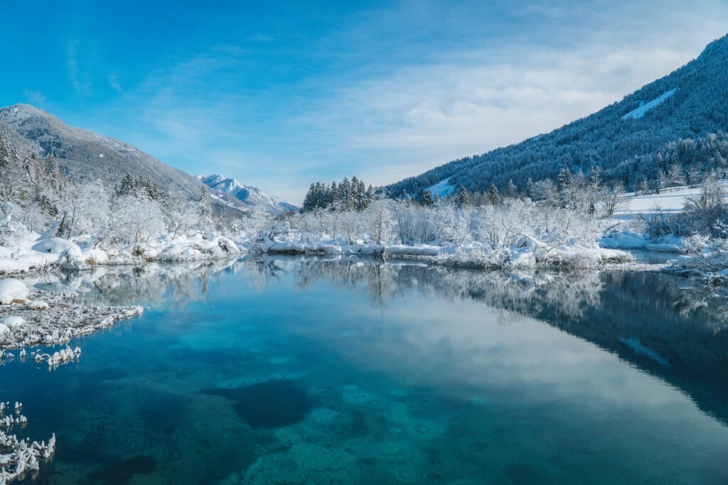 Crystal clear lake reflecting snow-covered trees and mountains under vivid blue winter sky Wallpaper