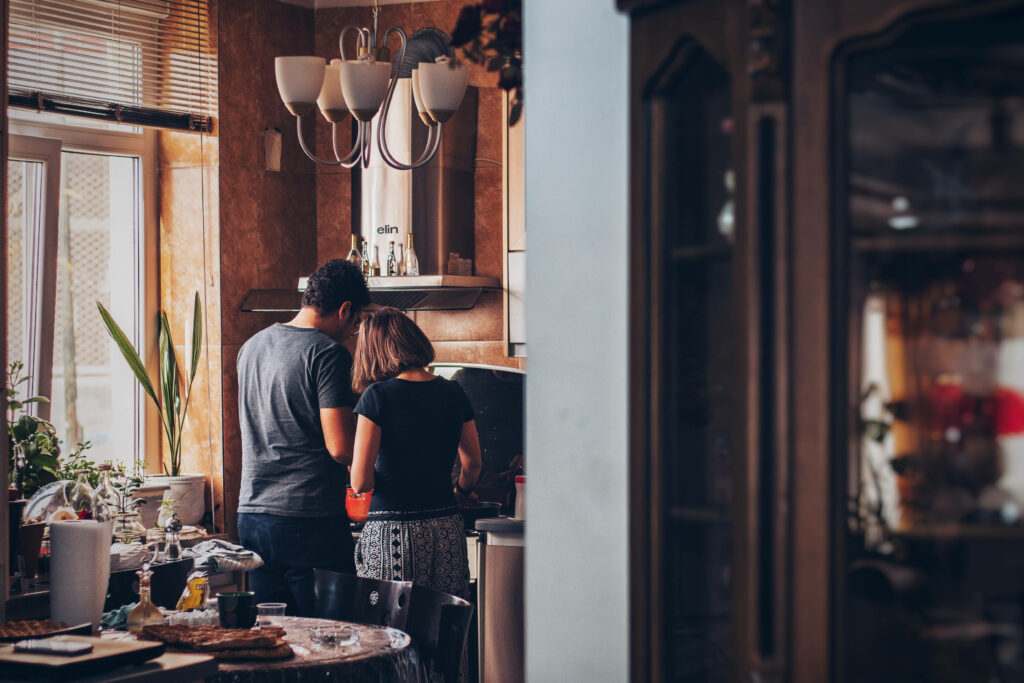 In the Heart of the Home: A Charming Snapshot of a Cooking Duo Nurturing Their Culinary Love in a Delightfully Adorned Kitchen Wallpaper