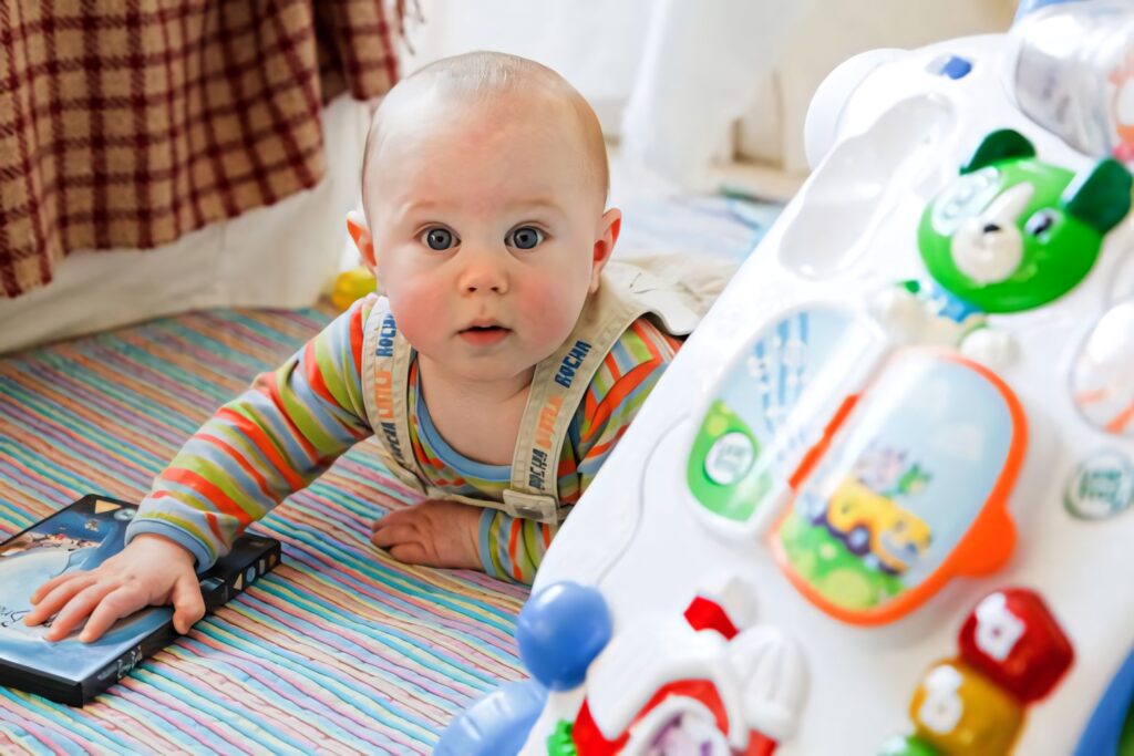 Baby boy in colorful clothes crawling on striped floor reaching for book near toys wallpaper