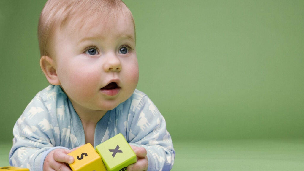 Curious baby boy in blue outfit playing with colorful letter blocks on soft green background Wallpaper