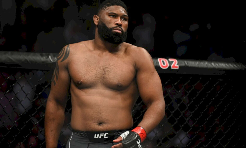 Curtis Blaydes in octagon showing athletic physique and focused expression under arena lighting Wallpaper