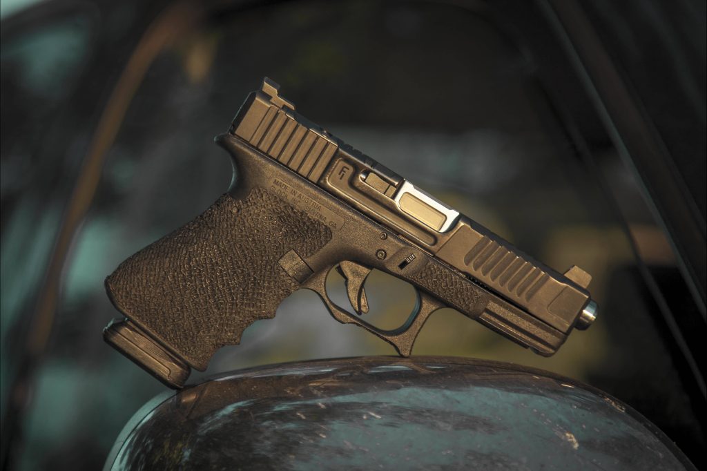 Customized Glock pistol with stippled grip and aftermarket slide on dark outdoor background Wallpaper