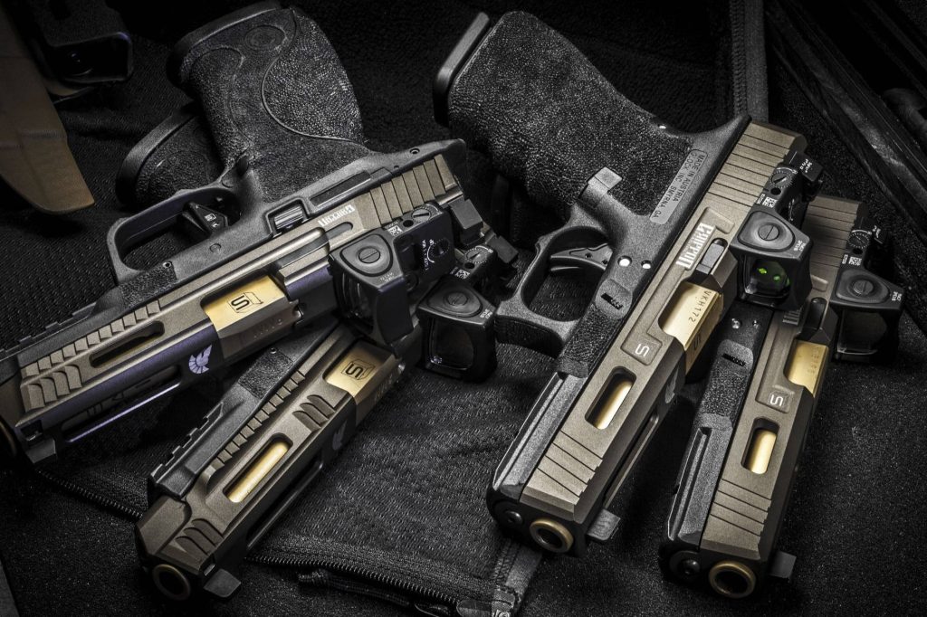 High-resolution wallpaper of four custom tactical pistols Glock Smith Wesson M&P with gold barrels and Trijicon RMR optics on black mat