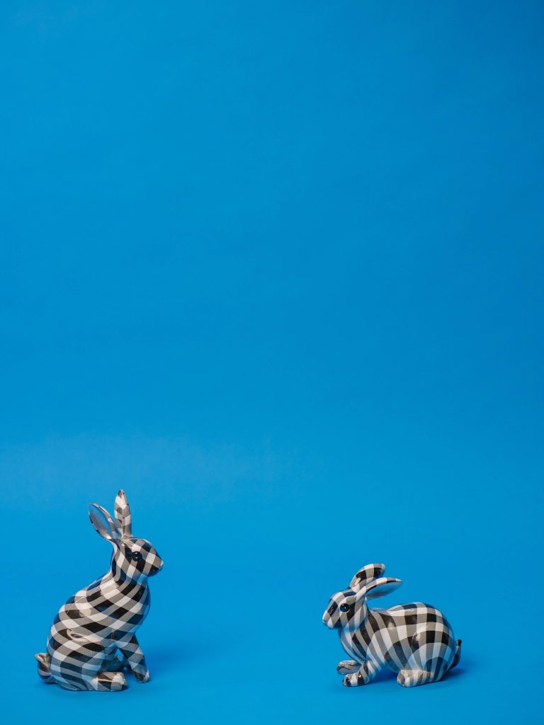 Blue wallpaper with two black and white checkered decorative rabbit figurines minimalist design