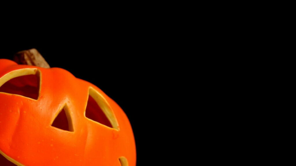 Cute and Creepy: HD Orange Pumpkin Face Against Black Background - Perfect Halloween Wallpaper!