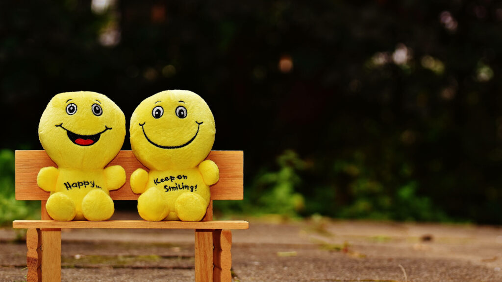 Cute Smile Duo: Cheerful Yellow Emoji Plush Toys Basking in the Warmth of a Wooden Bench Wallpaper