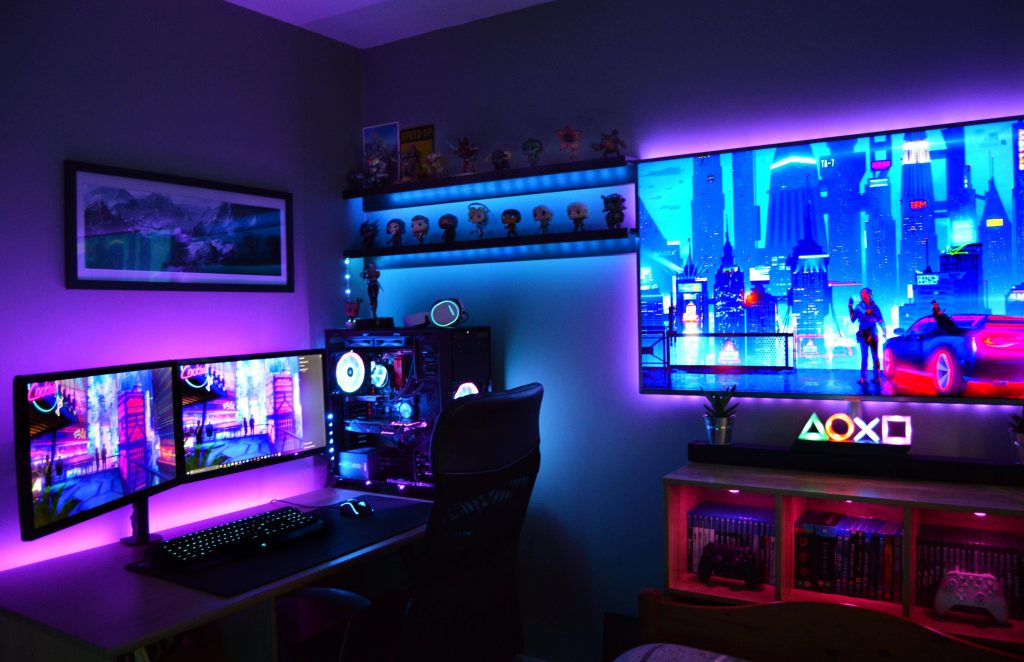 Cyberpunk gaming room with dual monitors custom PC blue purple RGB shelves Funko Pop figures Wallpaper