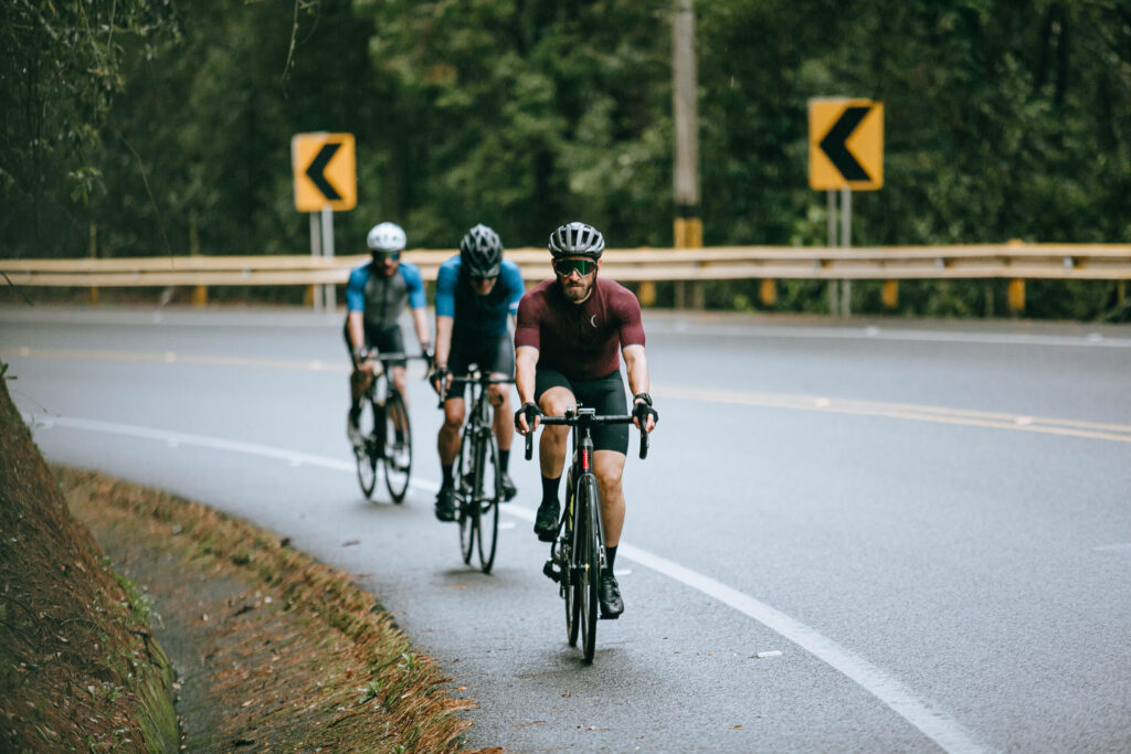 Three men in cycling gear ride on winding forest road showcasing teamwork endurance and adventure Wallpaper