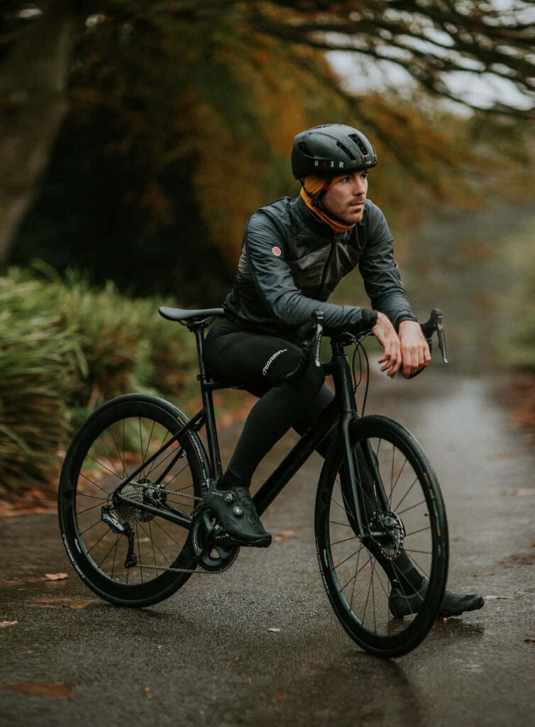 Cyclist in black gear pauses on wet leafy autumn path surrounded by lush green forest wallpaper