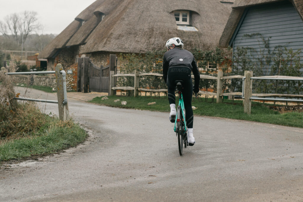 Cyclist rides past thatched cottage on rural lane with wooden fences and lush greenery wallpaper