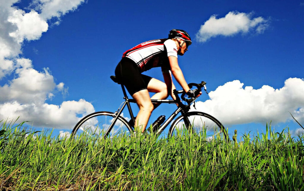 Cyclist in professional gear rides through green grass under blue sky with white clouds outdoor adventure Wallpaper