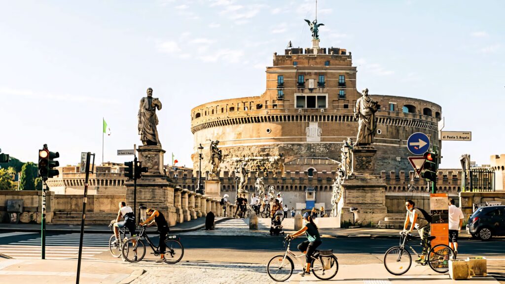 Cyclists biking near Castel Sant Angelo Rome warm sunlight historic statues vibrant cityscape wallpaper