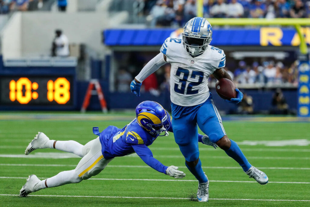 D'Andre Swift in Detroit Lions uniform evades tackle by LA Rams defender on green field game action Wallpaper