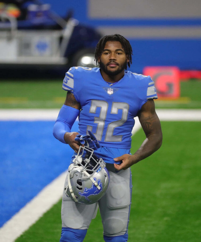 DAndre Swift in blue Detroit Lions jersey number 32 holds helmet confidently on football field Wallpaper