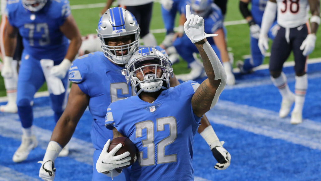 DAndre Swift celebrates Detroit Lions touchdown in blue silver uniforms on stadium turf background Wallpaper
