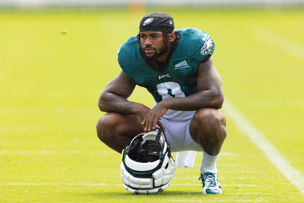 DAndre Swift kneeling on green football field in Philadelphia Eagles uniform holding helmet during practice Wallpaper