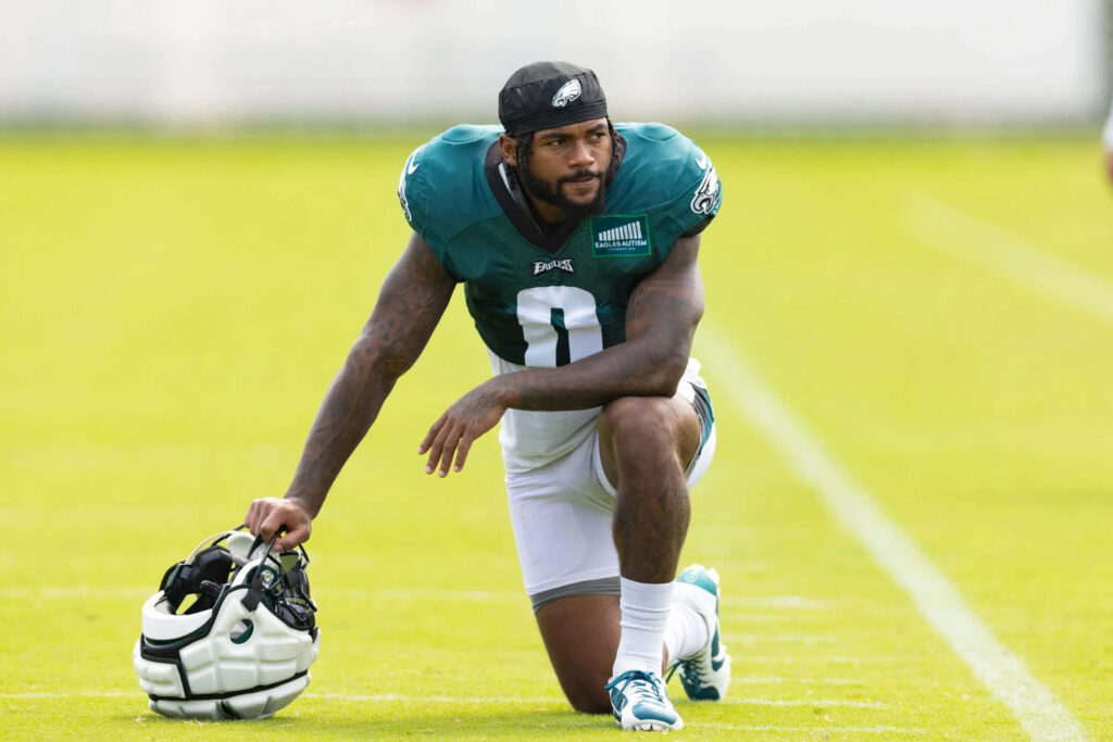 D'Andre Swift stretching on green football field in Philadelphia Eagles uniform with helmet in hand Wallpaper
