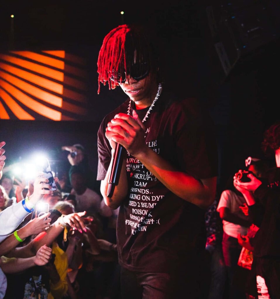 DC The Don rapping live under red purple lights with red-tipped dreads sunglasses and bold streetwear Wallpaper