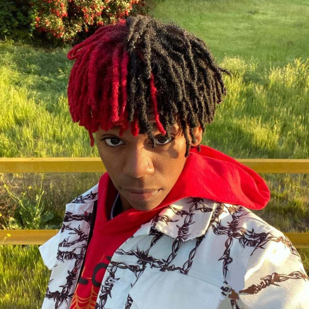 DC The Don in sunlight with red and black dreadlocks wearing bold jacket outdoors wallpaper background