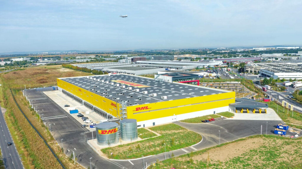 DHL Express Paris warehouse with bright yellow red building open space airplane ascending clear sky Wallpaper