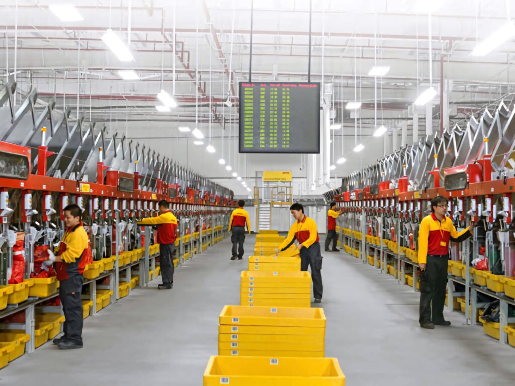 DHL team in yellow red uniforms sorting packages in modern logistics facility with advanced technology Wallpaper