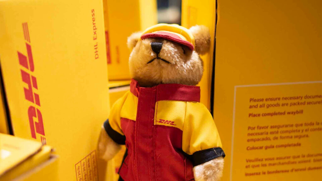 Plush DHL teddy bear in red yellow uniform among bright yellow DHL delivery boxes wallpaper background