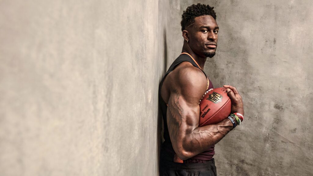 DK Metcalf holding football with muscular arms against gray wall showcasing athletic strength Wallpaper