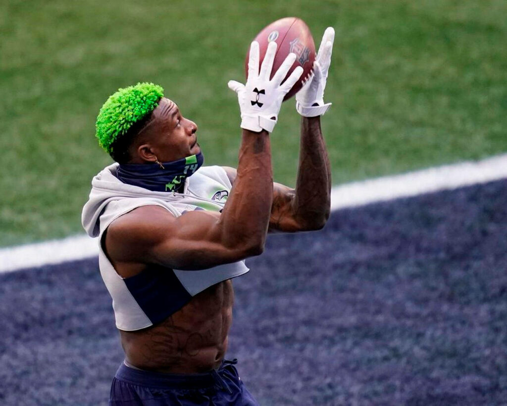 DK Metcalf in Seahawks hoodie with neon green hair focuses on catching football during practice Wallpaper