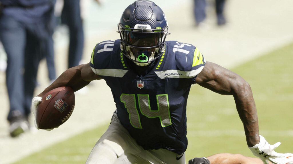 DK Metcalf in black Seahawks uniform gripping football showing power speed and focus action Wallpaper