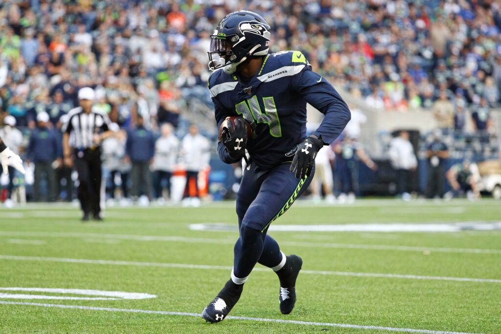 DK Metcalf in blue Seattle Seahawks uniform making dynamic play on vibrant football field background Wallpaper