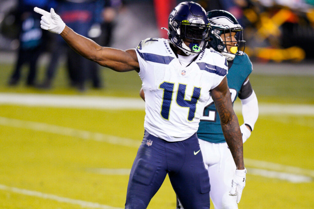 DK Metcalf in white Seattle Seahawks jersey number 14 running on green turf in action game Wallpaper