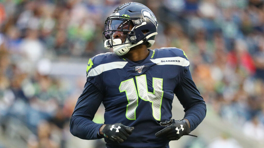 DK Metcalf in Seattle Seahawks uniform mid-game with vibrant stadium and team colors background Wallpaper