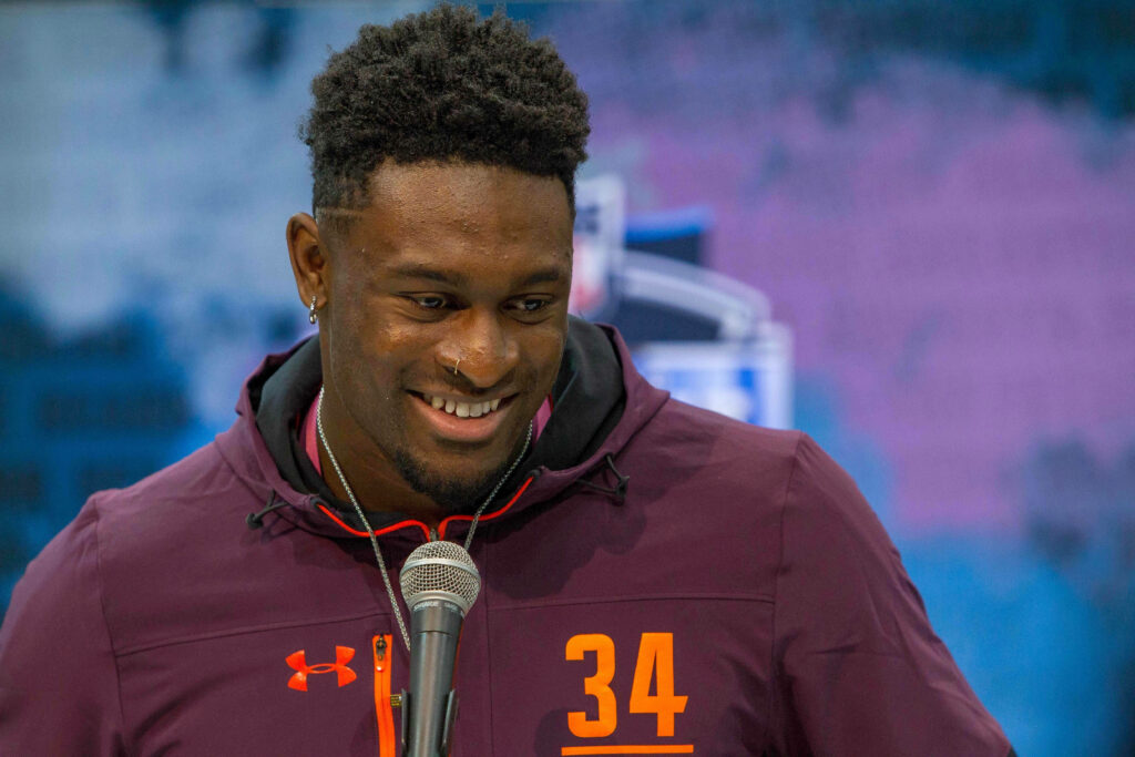 DK Metcalf smiling in maroon jacket number 34 at press event with blue purple backdrop wallpaper